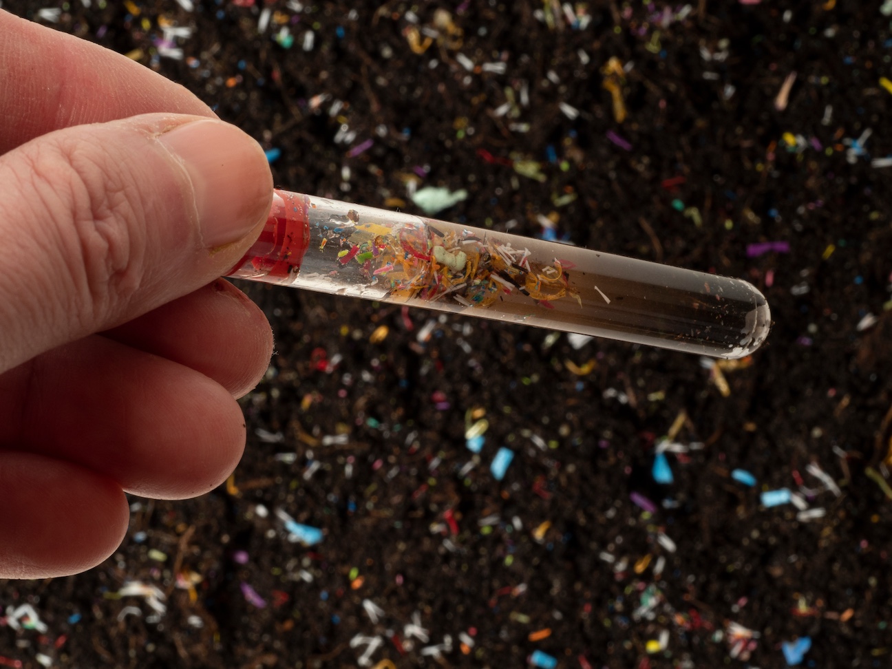 Person holding a test tube sample displaying tiny particles of plastic inside.